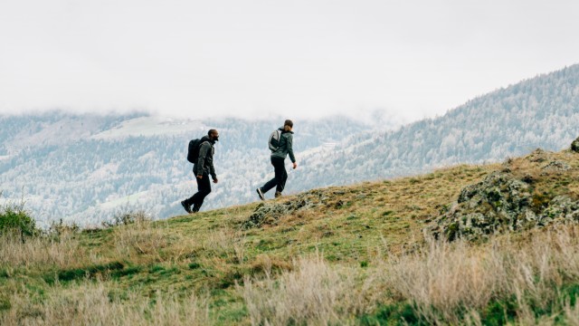 Une femme en tenue outdoor estivale en équilibre sur des pierres au bord d’un lac