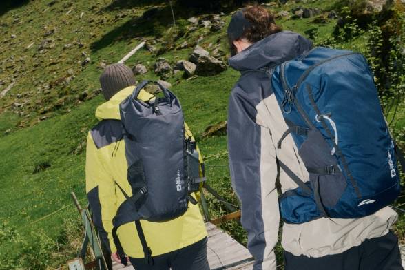 Deux randonneurs vus de dos avec des sacs à dos traversant un pont en bois