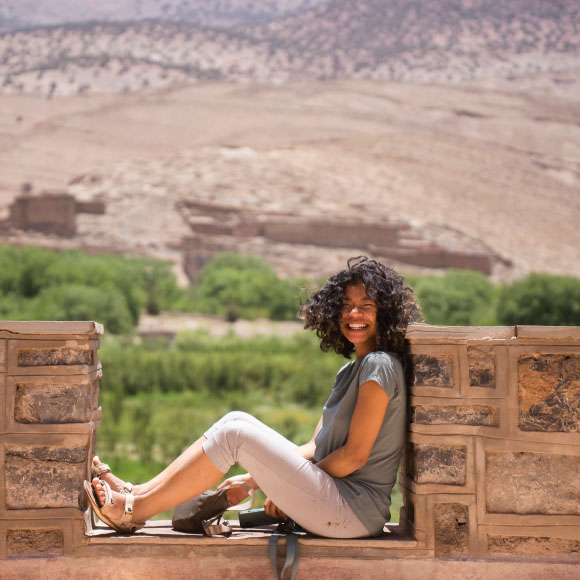 Isi assise sur un mur devant un paysage aride