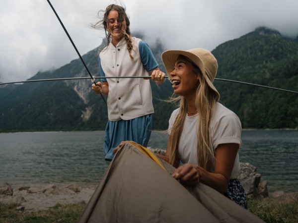 Deux femmes en train de rire et de monter une tente dans un paysage montagneux