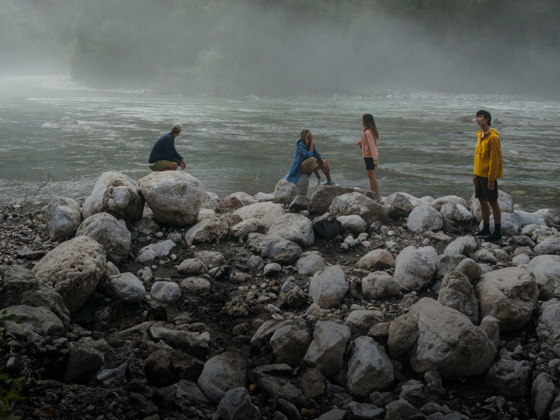 Un paysage avec une rivière dans le brouillard et 4 personnes sur des rochers devant