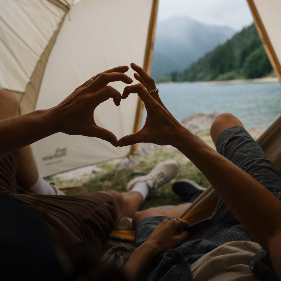 Deux personnes allongées dans une tente formant un cœur ensemble avec leurs mains